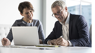 Smiling business woman and man reviewing laptop and making notes. Sandy Spring Bank Business Title Advantage.